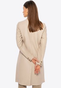 Beige leren jas met een getailleerde pasvorm, lange mouwen en details met een rugventilatie. Voorzien van knoopsluitingen bij de manchet en een soepele textuur.