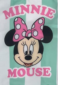 Illustratie van Minnie Mouse met grote zwarte oren en een roze stippenstrik op een witte achtergrond met mintgroene strepen en roze tekst.