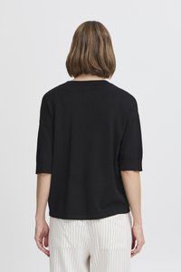 Czarny sweter z krótkim rękawem o luźnym kroju i prążkowanym dekoltem, zestawiony z spodniami w prążki, pokazany od tyłu.