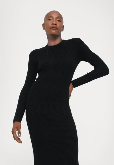 Rochie tricotată neagră, cu dungi, cu mâneci lungi și decolteu rotund. Siluetă ajustată și țesătură texturată. Fără modele sau accesorii distincte.