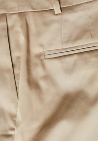 Beżowe spodnie w kant wykonane z gładkiego materiału, z jedną tylną kieszenią o płaskim designie oraz starannie wyprasowanymi liniami.