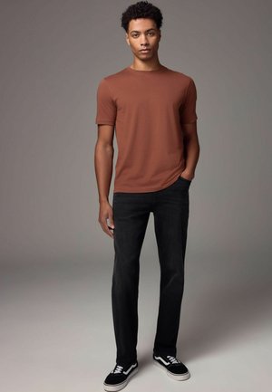 Hnedé tričko s krátkym rukávom, čierne slim-fit džínsy a čierne tenisky s bielymi detailmi. Hladká textúra a jednoduchý dizajn.