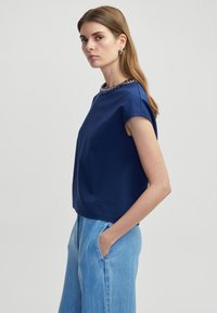 Marineblauw T-shirt met korte mouwen en een geprofileerde, versierde halslijn. Glad materiaal, boxy pasvorm, gecombineerd met lichtblauwe broek.