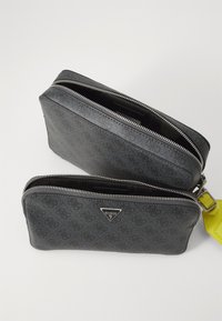 Conjunto de bolsas de cuero sintético negro con un brillante zipper plateado, que presenta un patrón de logo texturizado y un acento de strap amarillo.