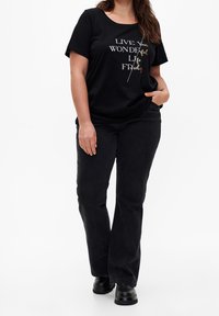 Sort t-shirt med korte ærmer og trykt budskab i hvidt og guld. Sammenkoblet med sorte brede jeans og sorte støvler.