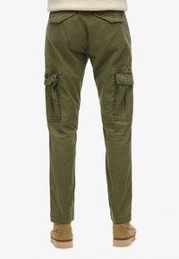 Olijf groene cargobroek met een slim fit, voorzien van twee zijzakken en opgevouwen kleppen. Gemaakt van duurzaam katoen. De schoenen zijn beige.