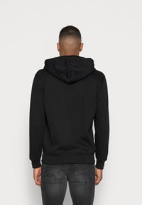 Svart huvtröja i mjukt material, med dragsko i huvan, långa ärmar och ribbad fåll. Strukturerad tyg med minimala detaljer.