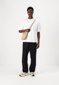 White oversized t-shirt, dark loose-fitting pants with pockets, tan crossbody bag, and beige sneakers with black accents. Simple styling.