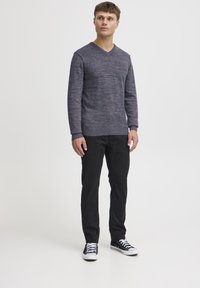 Maglione navy a maglia con scollatura a V, tessuto texturizzato e orlo a coste, abbinato a pantaloni neri e sneaker nere con suola bianca.