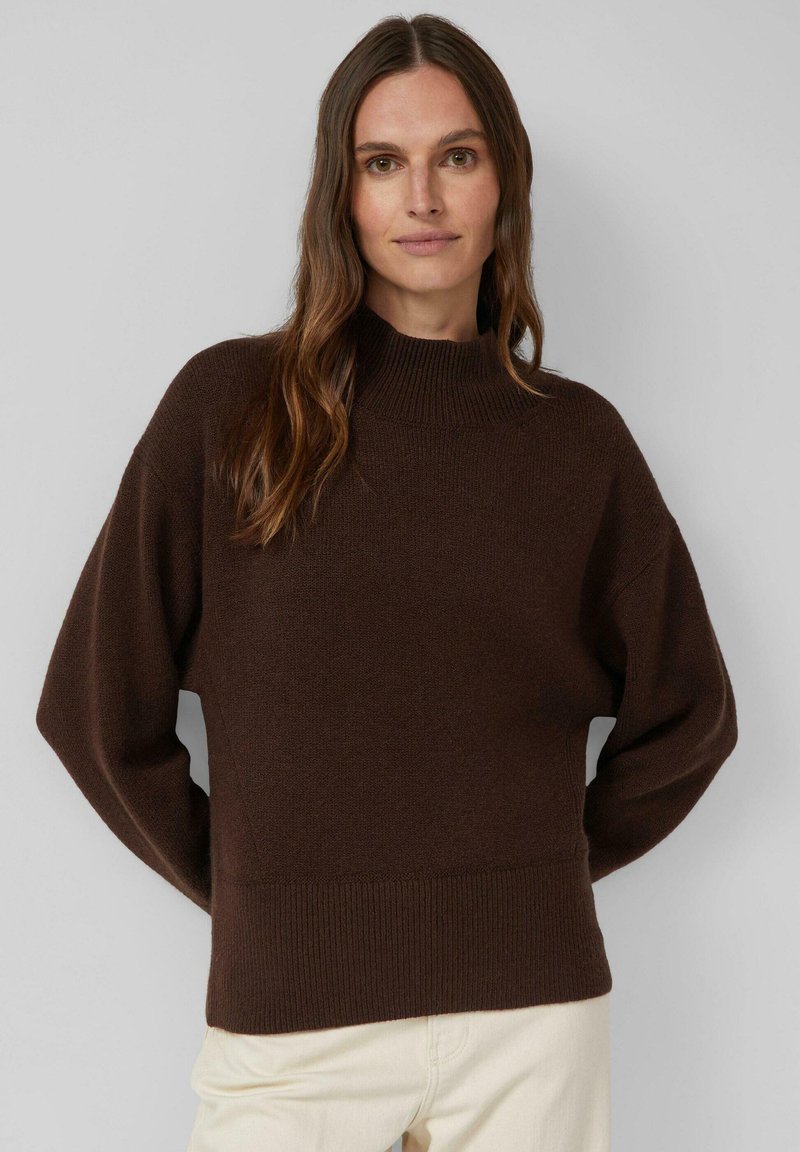 Brauner gestrickter Pullover mit hohem Kragen und lockeren Ärmeln. Verfügt über einen gerippten Saum und eine strukturierte Stoffoberfläche, getragen zu hellen Hosen.