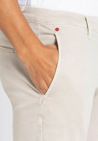 Beige pants featuring a front pocket with a red accent button, made of soft, textured fabric, highlighting stitching details on the seams.