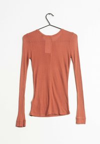 Långärmad topp i terracotta ribbat tyg, med rund halsringning, smal passform och en liten patchdetalj på framsidan.