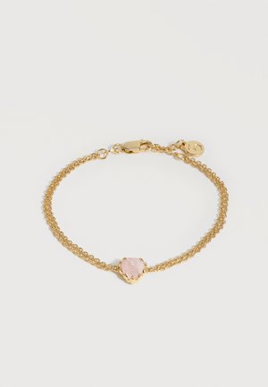 Λεπτό βραχιόλι με διπλή χρυσή αλυσίδα, κεντρικό στοιχείο ένα ροζ πολύτιμο λίθο σε σχήμα καρδιάς και μια μικρή στρογγυλή χρυσή ταμπελίτσα κοντά στο κούμπωμα.