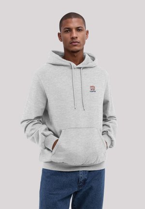 Grau Hoodie aus weichem Material, mit einer Fronttasche und besticktem Logodetail. Kombiniert mit dunkelblauen Jeans.