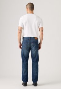 Jeans blu scuro con design a gamba dritta, dotati di tasche posteriori e di una toppa con logo in pelle. Indossati con una maglietta bianca semplice e scarpe nere.