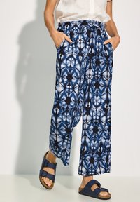 Blue and white patterned, wide-leg pants with a drawstring waist and side pockets, paired with dark blue sandals.