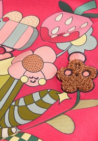 Tissu rose vif avec des fleurs colorées et stylisées, y compris une fleur marron crochetée avec des détails noirs et roses.