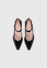 Black leather pointed-toe shoes with a strap and buckle detail. Smooth finish with a contrasting beige insole. Flat heel design.