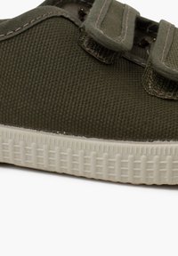 Olive green canvas shoe with Velcro straps, textured upper, and a white rubber sole featuring a patterned tread for grip.