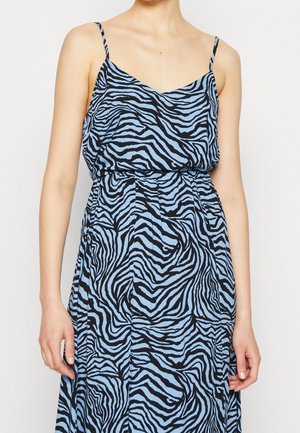 Femme portant une robe sans manches avec de fines bretelles et un motif zébré bleu et noir.