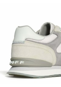 Zapatilla gris claro hecha de materiales de ante y cuero, con forma redondeada, cuello acolchado y suela media blanca con un logotipo en relieve.