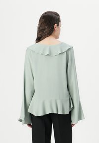 Mintgrønn bluse med volangkrage og utsvingte ermer. Laget av mykt stoff, har den en løs passform med lagdelt nederkant.