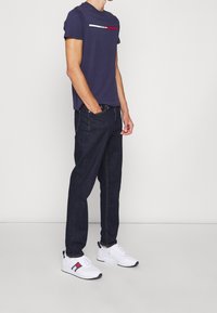 Námořnické tričko s vodorovným bílým a červeným pruhem, kombinované s tmavě modrými džíny a bílými teniskami s barevnými akcenty.