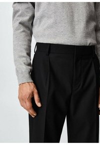 Zwarte op maat gemaakte broek met plissee, gecombineerd met een lichtgrijs lang mouwenk shirt. Glad stoffen textuur en standaard tailleband ontwerp.