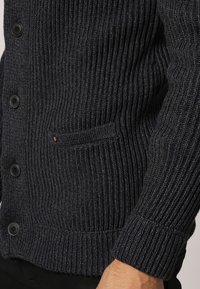 Mörk marinblå ribbade cardigan i strukturerad stickad kvalitet, med svarta knappar och en liten ficka på vänster sida.