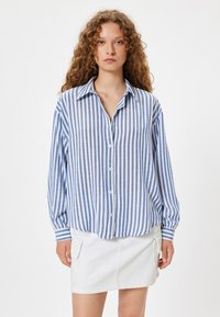 Blauw-wit gestreepte blouse met lange mouwen en een kraag, gecombineerd met een witte denimrok met zijzakken.