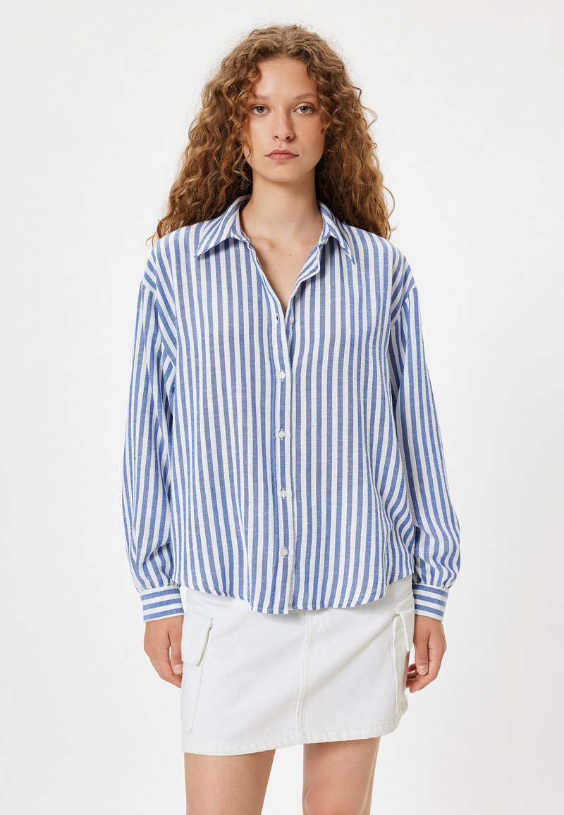 Blauw-wit gestreepte blouse met lange mouwen en een kraag, gecombineerd met een witte denimrok met zijzakken.