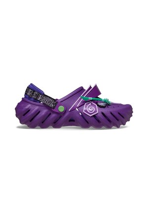 Purple Crocs clog with a strap, textured sole, and decorative charms including a spiral, flag, and arrow on the upper side.