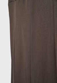Gros plan sur un tissu marron avec des coutures verticales sur un vêtement, montrant une texture lisse et des détails de couture subtils.
