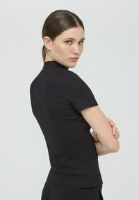 Czarny krótki top z krótkim rękawem o wysokim dekolcie, prążkowanej fakturze i dopasowanym kroju, charakteryzujący się prostym wzornictwem.