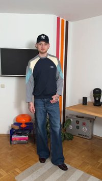 Sweatshirt azul-marinho com mangas em blocos de cor em azul claro, cinza e amarelo pálido. Combinado com jeans de ganga com boca larga e sapatos escuros.