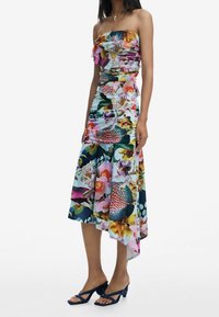 Robe florale sans bretelles avec un haut à volants, design froncé, motifs de fleurs colorés, ourlet asymétrique, accompagnée de sandales à talons bleues.