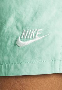 Shorts Nike en tissu vert menthe clair, avec un logo brodé blanc, texture lisse et détail de couture contrastante au niveau de l'ourlet.
