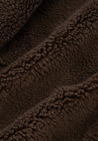 Bruin pluche stof met een zachte, pluizige textuur, voorzien van een diepe pool en een glad oppervlak, geschikt voor knusse kleding of huistextiel.