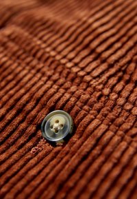 Bruin corduroy stof met verticale ribbels en een grote, ronde, transparante knop in het midden.