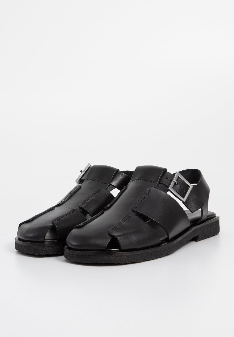 Zwarte leren sandalen met open teen en uitsnijdingen. Voorzien van een zilveren gesp en een gestructureerde zool. Platte profiel met een minimalistisch ontwerp.