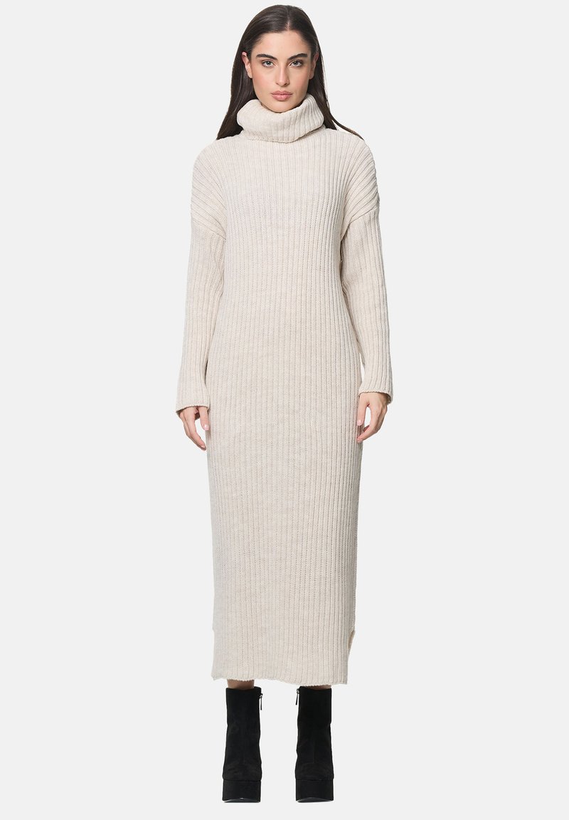 Langes beiges Rippstrickkleid mit Rollkragen, langen Ärmeln und Seitenschlitzen, kombiniert mit schwarzen Absatz-Ankle-Boots.