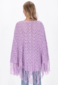 Lavendelfärgad stickad poncho med öppen chevronmönster och fransar nertill. Lätt och löst sittande design, lämplig för att bära i lager.