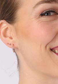 Silberne Creolen und zwei kleine Steckerohrringe, die am Ohr eines Models präsentiert werden; mit glänzender Oberfläche und minimalistischen Design.