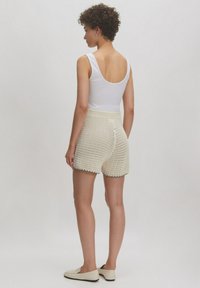 Crème gebreide shorts met een textuurdesign, elastische tailleband en zwarte rand aan de zoom, gecombineerd met een witte tanktop en lichte schoenen.