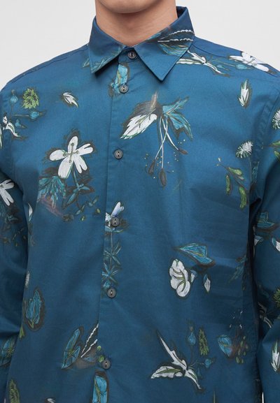 Homme portant une chemise boutonnée sarcelle avec col et motifs floraux blancs et verts.