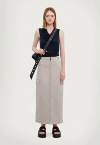 Haut bleu marine à col cheminée associé à une jupe cargo beige clair avec une fermeture éclair à l'avant et des poches latérales. Sandales noires avec des brides épaisses.