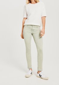 Jeans skinny verde claro con una textura suave, combinados con una camiseta blanca de manga corta con canalé y zapatillas blancas con detalles en negro.
