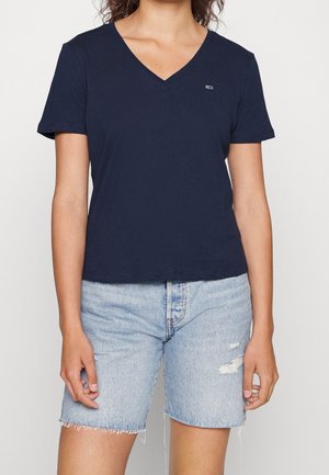 Kvinde iført en mørkeblå V-hals kortærmet T-shirt kombineret med lyseblå, let slidte denimshorts med små revner.