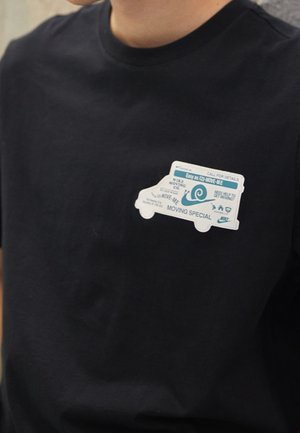 Osoba ubrana w czarną koszulkę z grafiką białej ciężarówki przeprowadzkowej i tekstem na piersi: „Moving Special” oraz „Potrzebujesz pomocy przy przeprowadzce?”.