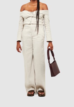 Off-white, off-the-shoulder topp med tvistad front och långa ärmar; matchande vida byxor. Håller en bourgogne, krokodilmönstrad handväska. Bruna sandaler.